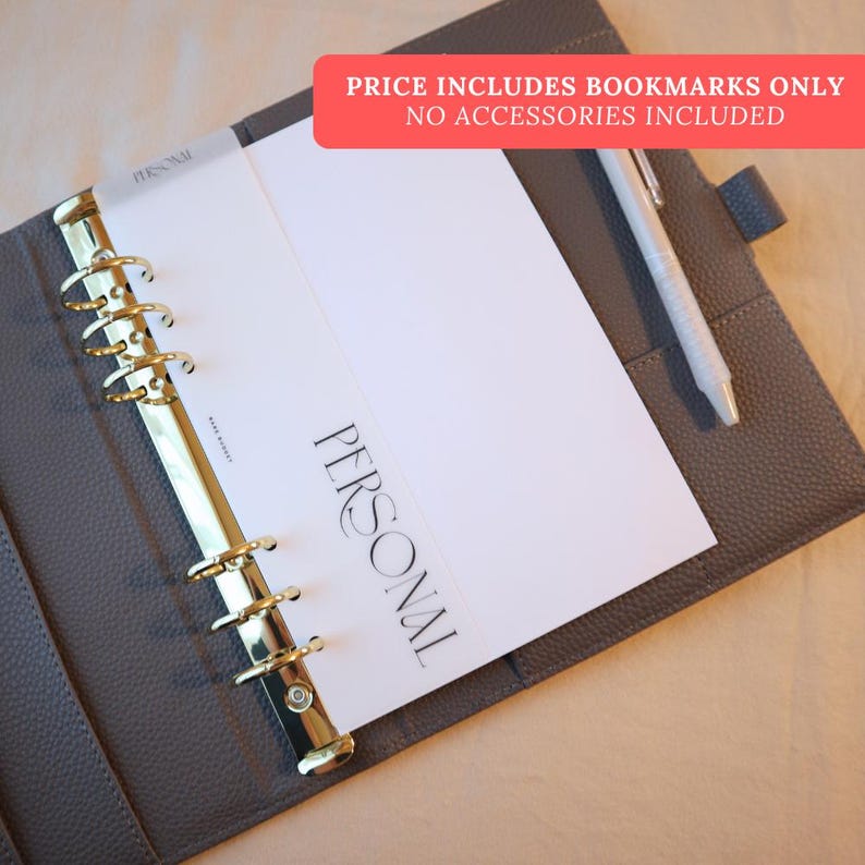 May include: A gray leather-like personal planner with gold-colored rings and a pen. The planner is open to a white page with the word "PERSONAL" printed on it. The text "PRICE INCLUDES BOOKMARKS ONLY NO ACCESSORIES INCLUDED" is in a red banner.