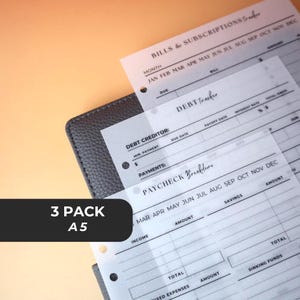 May include: A three-pack of A5-sized financial planning inserts. The translucent sheets include sections for bills, subscriptions, debt tracking, and paycheck breakdowns. The sheets are designed to fit into a planner and are shown against a gray planner.