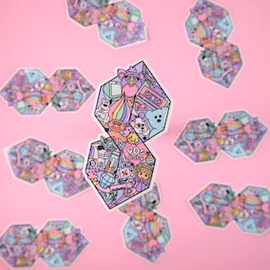 Pu&ograve; includere: Un adesivo con uno schema di colori rosa, blu e giallo che presenta una variet&agrave; di icone della cultura pop degli anni '90, tra cui una bambola troll, un Furby, un nastro per cassette e un arcobaleno. L'adesivo dice "90s Baby" al centro.