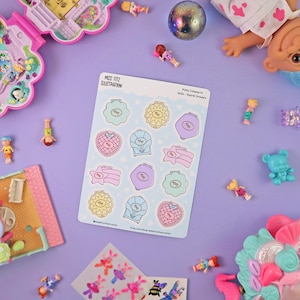 Könnte beinhalten: Ein Bogen Aufkleber mit pastellfarbenen Illustrationen von Vintage-Spielzeug-Kompakten. Der Bogen ist mit "Miss Fitz Illustration" und "Polly Compacts" beschriftet. Auf einer violetten Oberfläche sind weitere Spielzeuge und Accessoires verstreut.
