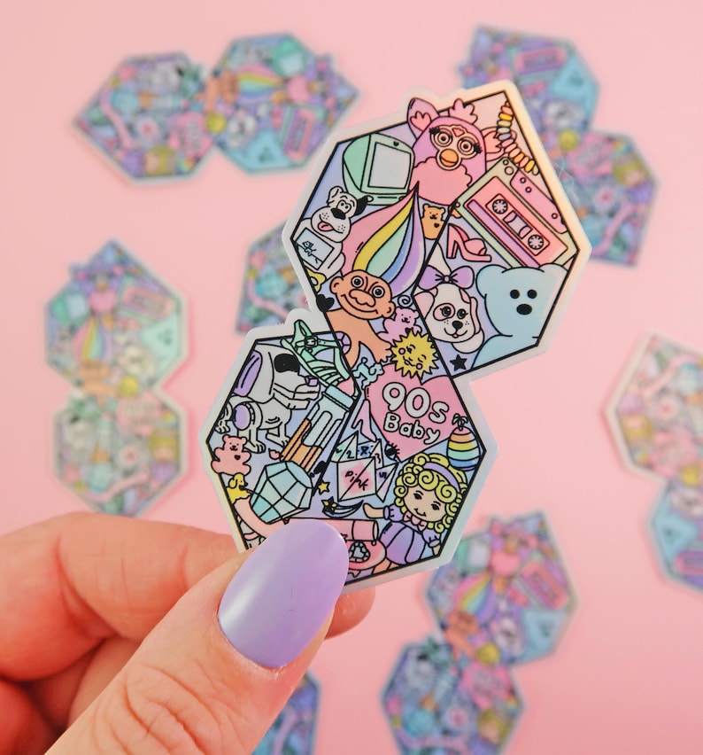Pu&ograve; includere: Due adesivi esagonali a tema anni '90. L'adesivo superiore presenta un troll con i capelli arcobaleno, una creatura rosa e pelosa, un nastro per cassette, un tacco alto e un orsacchiotto di peluche. L'adesivo inferiore presenta un bambino dei cartoni animati, un arcobaleno, un cristallo e un cuore rosa con il testo "90s Baby".