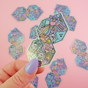 Pu&ograve; includere: Un set di nove adesivi olografici con una variet&agrave; di icone della cultura pop degli anni '90. Gli adesivi hanno la forma di esagoni e presentano una gamma di colori arcobaleno. Gli adesivi includono immagini di una bambola troll, un Tamagotchi, un nastro per cassette, un Furby e altro ancora.