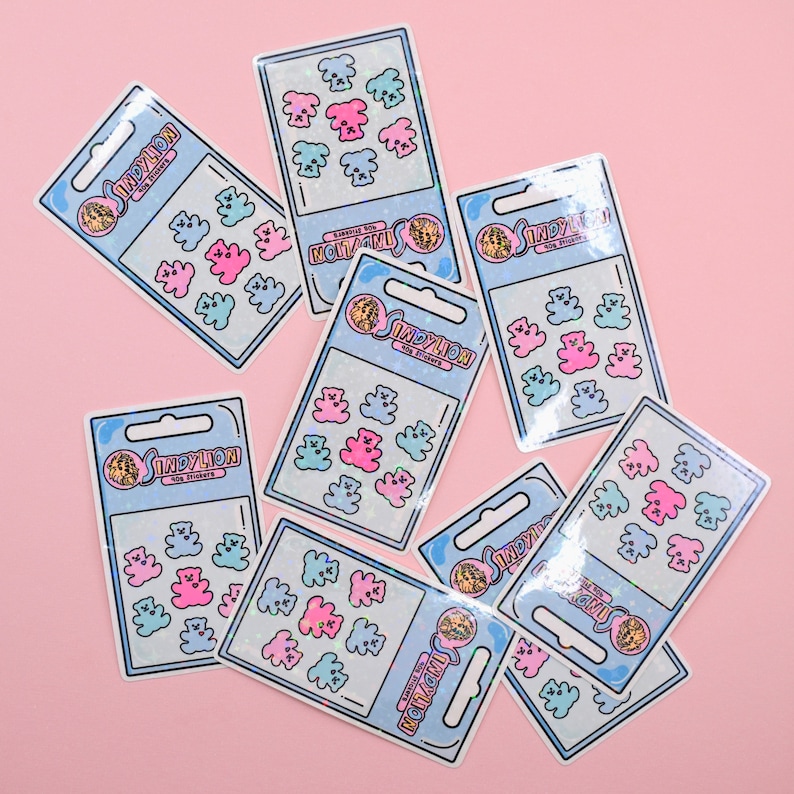 May include: A set of 10 colorful gummy bear stickers with a holographic finish. The stickers are arranged in a grid pattern on a pink background. The stickers feature the text "INDYLION" and "NOTAGMI".