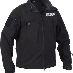 Op de afbeelding: Zwarte softshelljas met ritssluiting en een reflecterende "SECURITY" patch op de rechterborst. De jas heeft meerdere zakken, waaronder een grote zak op de linkerborst met een klep en een kleinere zak op de rechterborst.