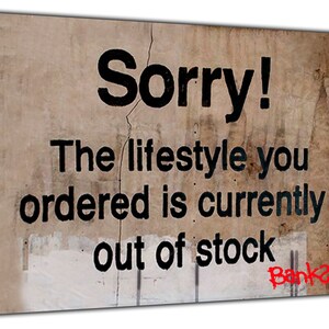 Könnte beinhalten: Ein verwitterter, beiger Hintergrund mit schwarzem Text, der "Sorry! Der Lebensstil, den Sie bestellt haben, ist derzeit nicht auf Lager." lautet. Der Text ist in Rot mit "Banksy" signiert.