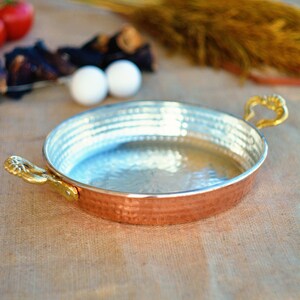 May include: A copper serving dish with two gold handles. The dish has a hammered finish and is sitting on a burlap surface.