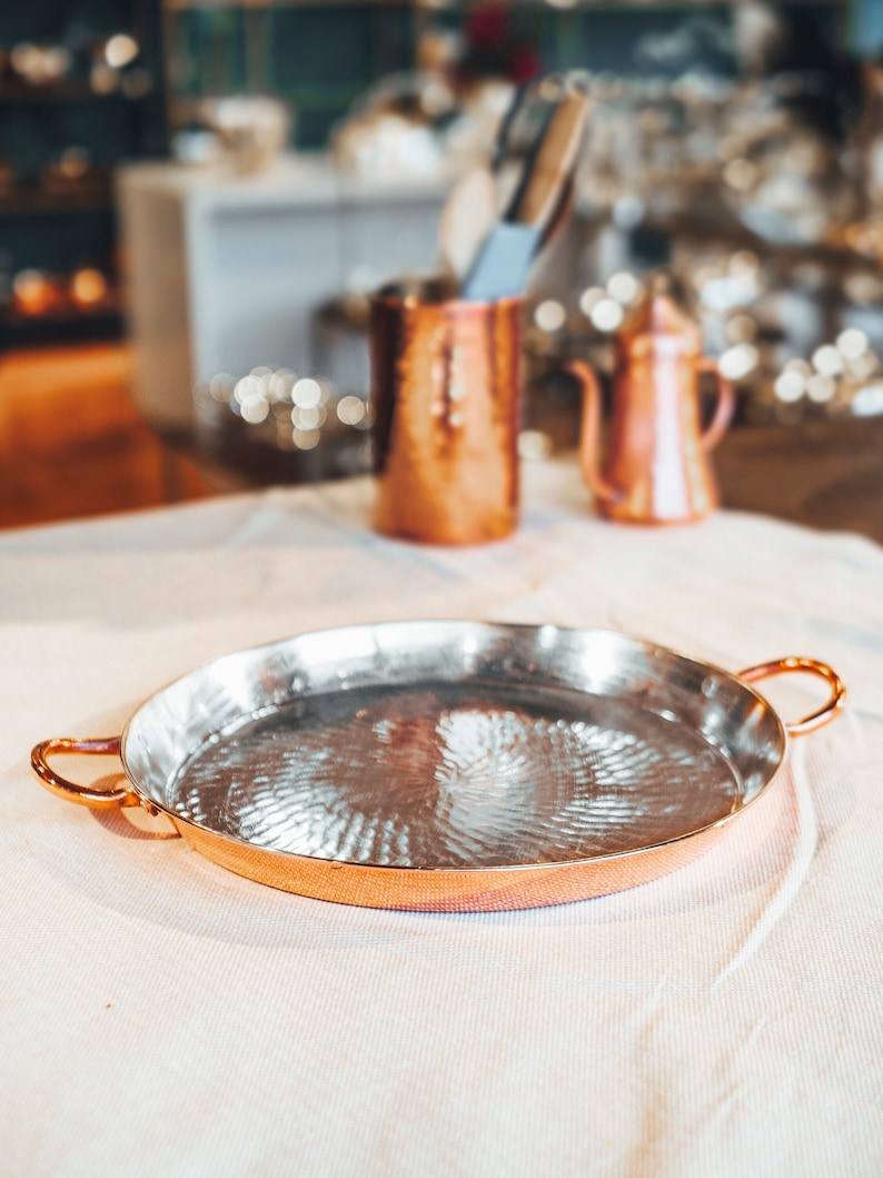 May include: A hammered copper serving tray with two handles. The tray is empty and has a shiny, reflective surface.