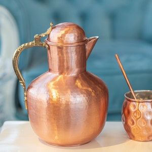 May include: A hammered copper pitcher with a brass handle and lid, and a matching hammered copper cup with a straw.