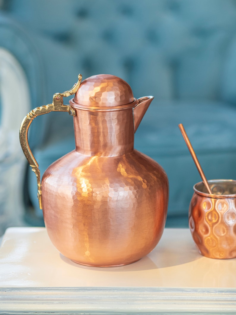 May include: A hammered copper pitcher with a brass handle and lid, and a matching hammered copper cup with a straw.