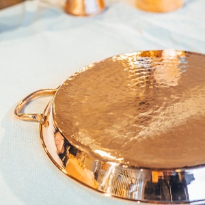 May include: A hammered copper serving tray with a single handle. The tray has a shiny, reflective surface.