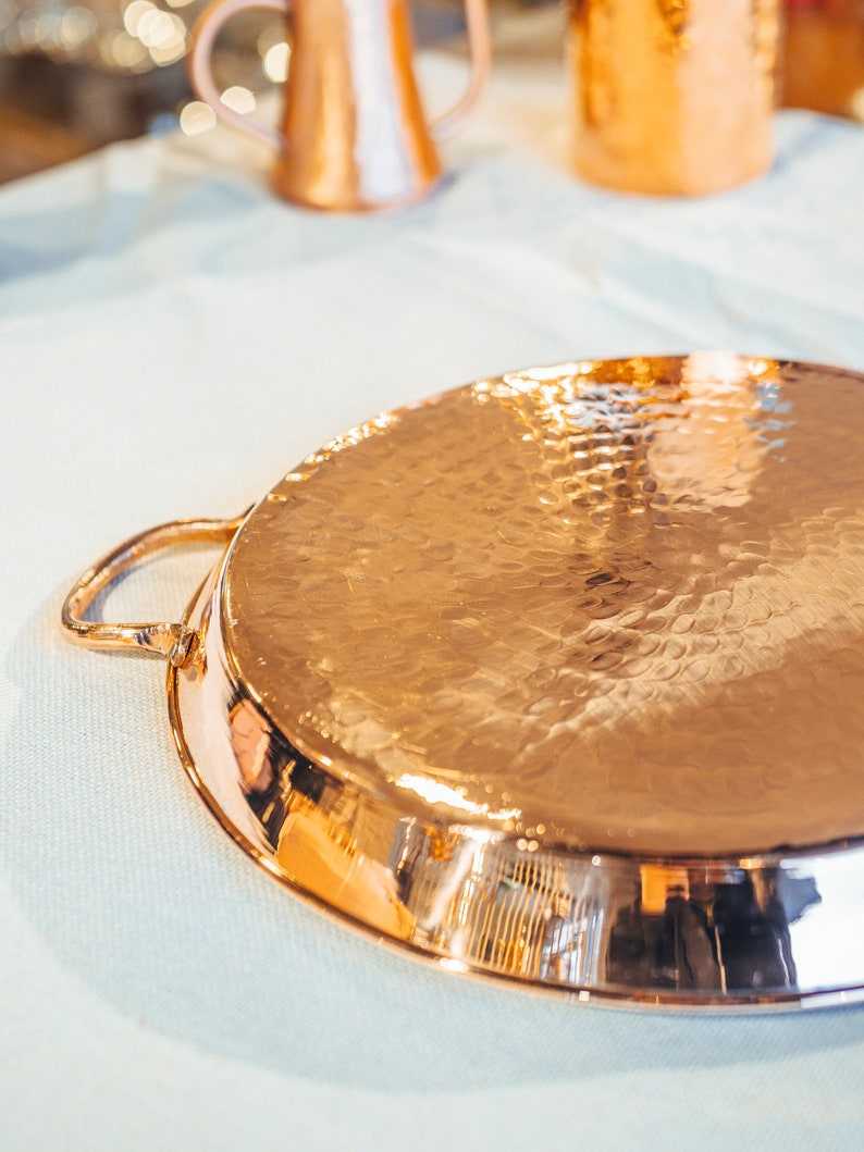 May include: A hammered copper serving tray with a single handle. The tray has a shiny, reflective surface.