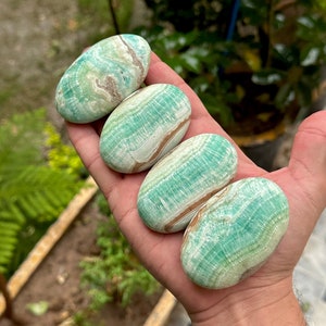May include: Four smooth, oval-shaped green and brown stones with swirling patterns. The stones are arranged in a row in a person's hand.