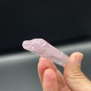 May include: A pale pink, translucent crystal with striations, resembling a long, thin shard.