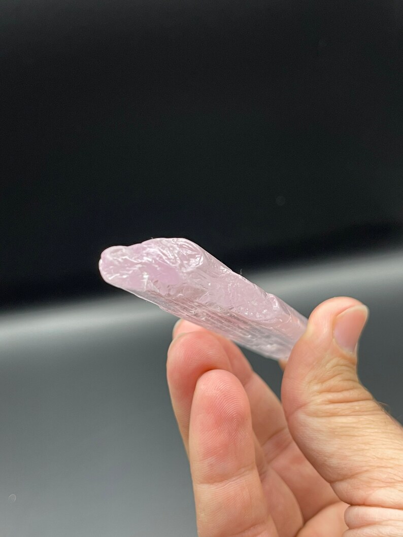May include: A pale pink, translucent crystal with striations, resembling a long, thin shard.