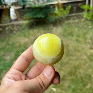 May include: A yellow and white sphere made of polished stone. The sphere is smooth and has a slightly translucent appearance.