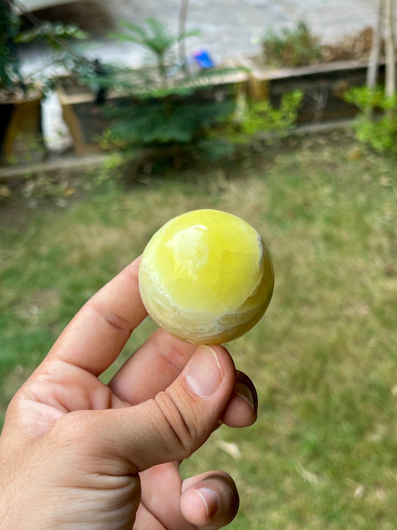 May include: A yellow and white sphere made of polished stone. The sphere is smooth and has a slightly translucent appearance.