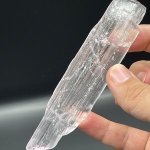 May include: A clear selenite crystal wand with a pointed tip and a smooth, polished surface. The crystal is translucent and has a slight pink hue.