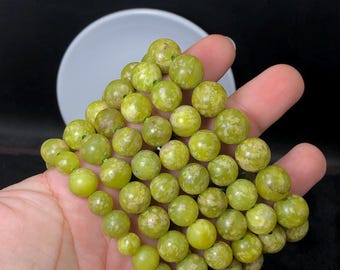 May include: A strand of green serpentine beads with white flecks. The beads are round and smooth.