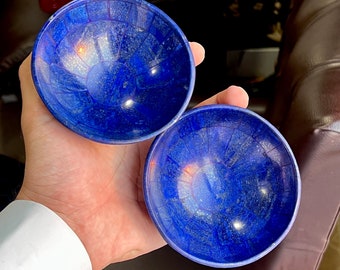 May include: Two small, round, blue bowls made of lapis lazuli. The bowls have a shiny, polished finish and are decorated with a swirling pattern.