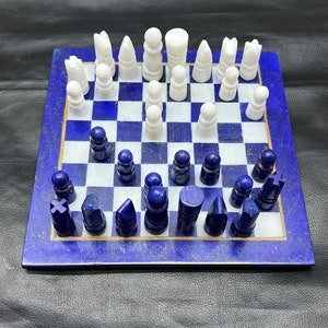 May include: A blue and white chess set with white pieces on a blue board. The board is made of lapis lazuli and has a gold trim. The pieces are made of white marble.