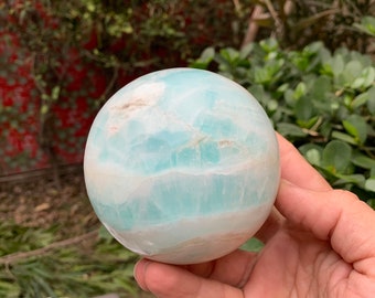 May include: A light blue and white sphere of polished Celestite, a crystal known for its calming energy. The sphere is smooth and has a swirling pattern.