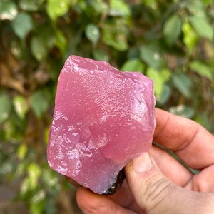 May include: A large, rough, pink crystal with a smooth, polished surface. The crystal is translucent and has a slight shimmer.