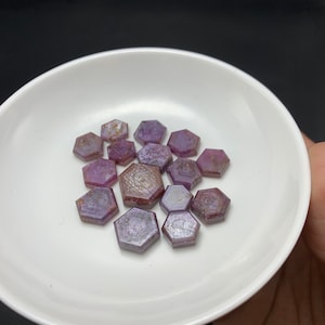 May include: A collection of purple and pink hexagonal shaped gemstones. The gemstones are faceted and have a shiny, polished finish.