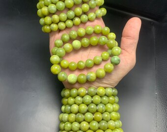 May include: Several strands of light green beaded bracelets are displayed on a hand. The bracelets are made of round, polished beads. The bracelets are a light green color, and the beads appear to be about 0.5 inches in diameter.