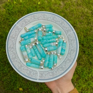 May include: A plate of aqua blue and silver pendant charms. The charms are made of polished aquamarine stone and have a silver bail.