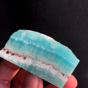 May include: A light blue and white banded polished piece of turquoise with a brown mineral vein running through it.