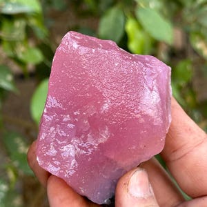 May include: A large, pink, rough-cut crystal with a smooth, polished surface. The crystal is translucent and has a slight purple hue.