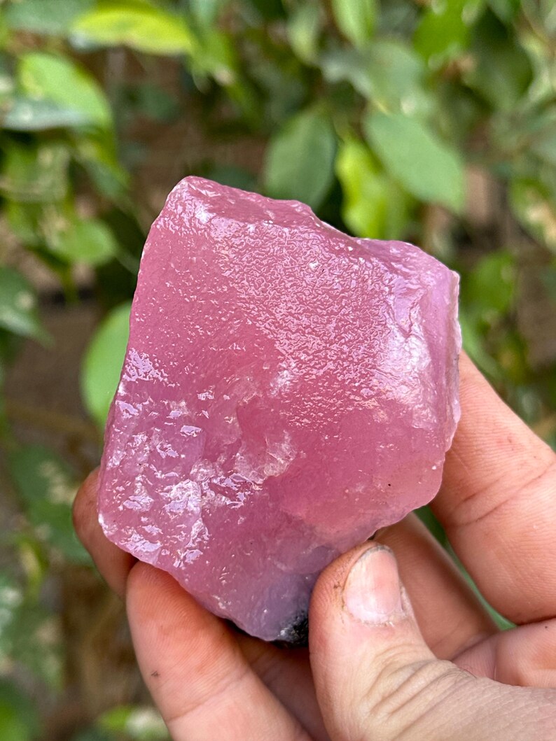 May include: A large, pink, rough-cut crystal with a smooth, polished surface. The crystal is translucent and has a slight purple hue.