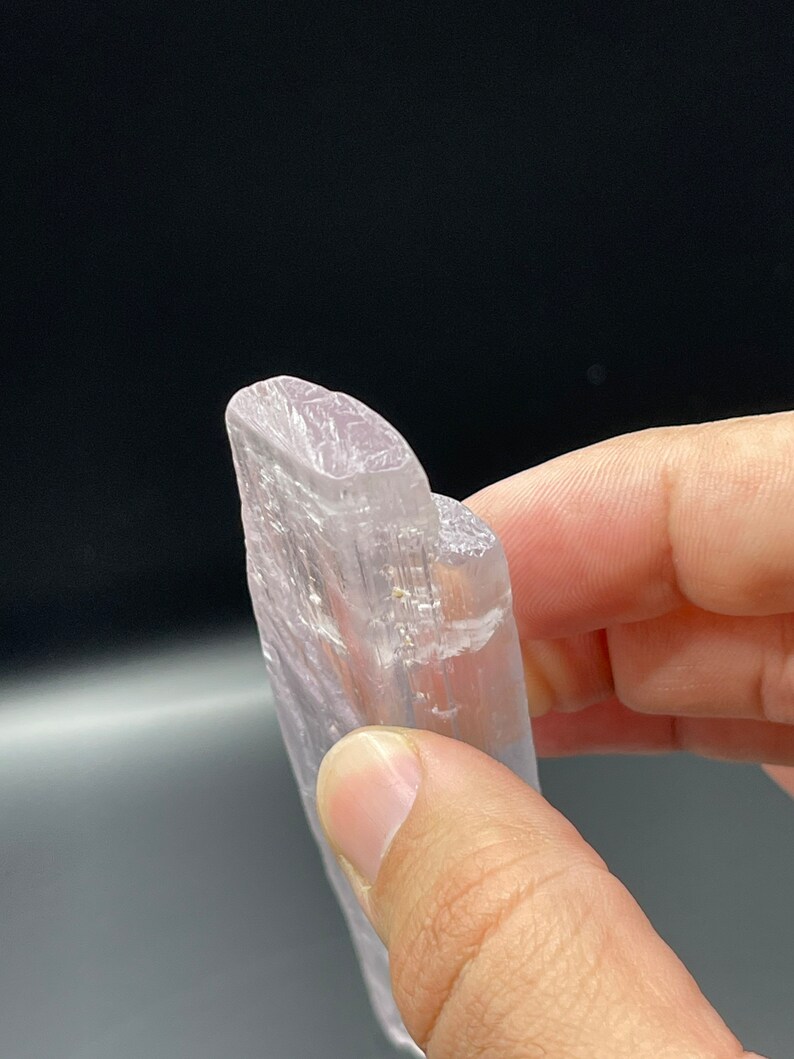 May include: A translucent white selenite crystal with a smooth, polished surface. The crystal is shaped like a long, thin blade and has a slightly rounded tip.
