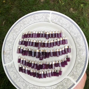 Può includere: Un piatto di ciondoli in pietra preziosa viola con cappucci d'argento. I ciondoli sono disposti in file e sono tutti della stessa dimensione e forma.