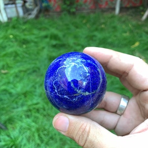 May include: A smooth, round, blue lapis lazuli sphere with white veins. The sphere is being held in a hand.