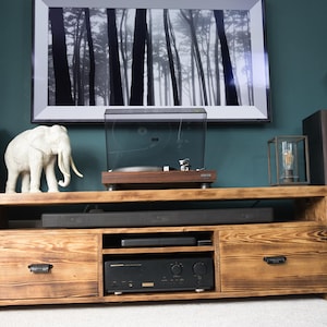 May include: A wooden entertainment center with a turntable, speakers, and a framed black and white forest print. A white elephant statue and a decorative lantern are on the top. The cabinet has two drawers and a lower shelf.