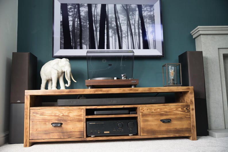 May include: A wooden entertainment center with a turntable, speakers, and a framed black and white forest print. A white elephant statue and a decorative lantern are on the top. The cabinet has two drawers and a lower shelf.