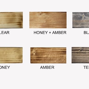 May include: A collection of six wooden planks, each showcasing a different stain color. The colors include Clear, Honey + Amber, Black, Honey, Amber, and Terra. The planks are rectangular and display the wood grain.