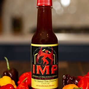 May include: A glass bottle of hot sauce with a red cap. The label is black with a red and yellow illustration of a devil holding a bottle of hot sauce. The label reads "IMP Internally Malicious Peppers Devil's Master The Sauce You Deserve! 5.75 FL OZ 2M Scoville Units (Hottest)". The bottle is surrounded by red, yellow, and brown chili peppers.