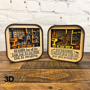 May include: Two wooden signs with a 3D design of tools. The sign on the left says "GRANDPA has all the tools, but it's his HUGS that fix everything." The sign on the right says "FATHERHOOD is letting your kids use your good screwdriver."