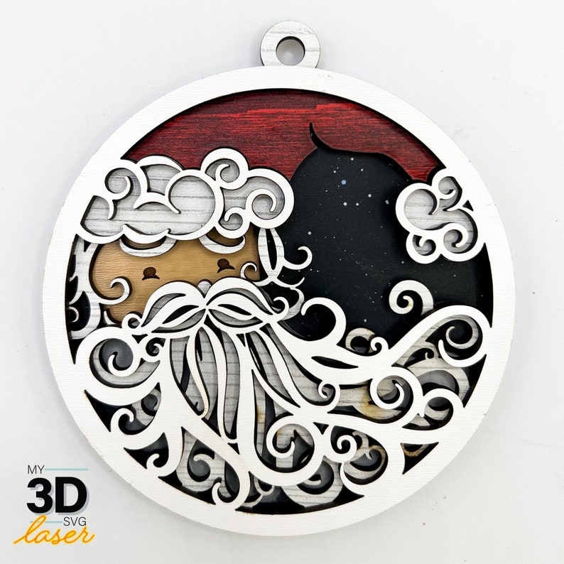 May include: A white wooden ornament with a black and white design of a Santa Claus face with a curly beard and a red and white striped hat. The ornament is round and has a hole at the top for hanging.