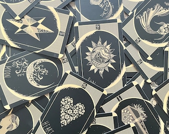 May include: A close-up of a deck of tarot cards with black backgrounds and gold accents. The cards feature various illustrations, including a crescent moon, a star, a heart, and a fish.