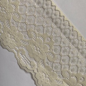 May include: Ivory lace trim with a delicate floral pattern. The lace has a scalloped edge and a diamond-shaped background.