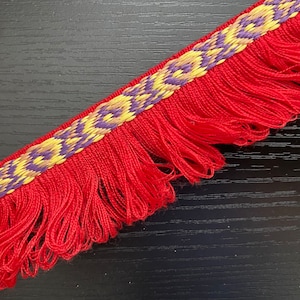 May include: Red fringe trim with a woven pattern in yellow, purple, and brown. The fringe is approximately 1 inch wide.