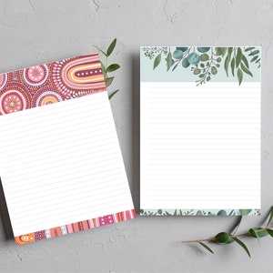 May include: Two lined notepads with different designs. One notepad has a pink, red and orange geometric pattern. The other notepad has a light blue background with a green leafy pattern.