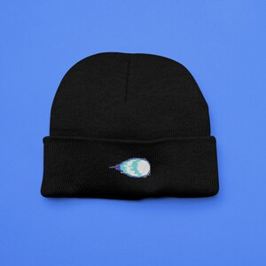 May include: Black knit beanie with a blue and white pixelated comet design embroidered on the front.