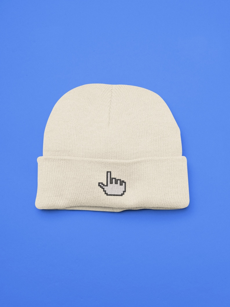 K&ouml;nnte beinhalten: Cremefarbene Beanie-M&uuml;tze mit einem pixeligen Handcursor-Design, das auf den umgeschlagenen Rand gestickt ist. Die M&uuml;tze besteht aus einem weichen Strickmaterial und liegt vor einem hellblauen Hintergrund. Ein schlichtes, modernes Accessoire.