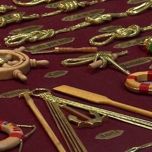 Side view of golden sailor's knots, miniature naval tools, golden cardboard labels and red fabric background.