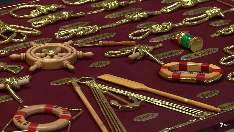 Side view of golden sailor's knots, miniature naval tools, golden cardboard labels and red fabric background.