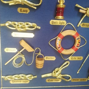 Detail view of table with golden knots and miniatures of naval tools, fabric background and golden cardboard labels.